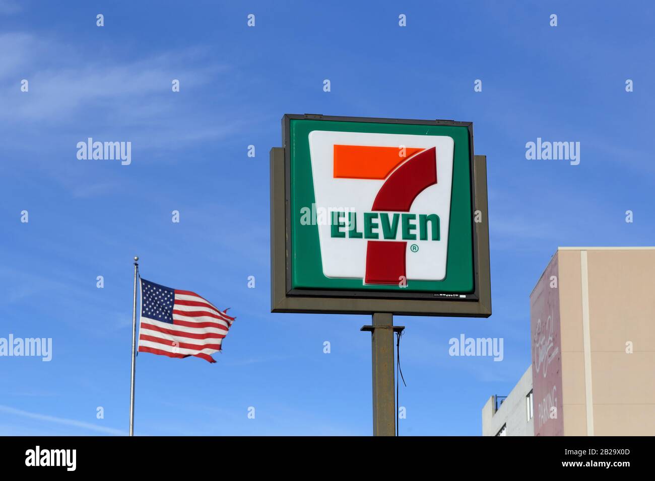 Un 7-Eleven segno su una pole contro uno sfondo blu cielo con bandiera americana Foto Stock