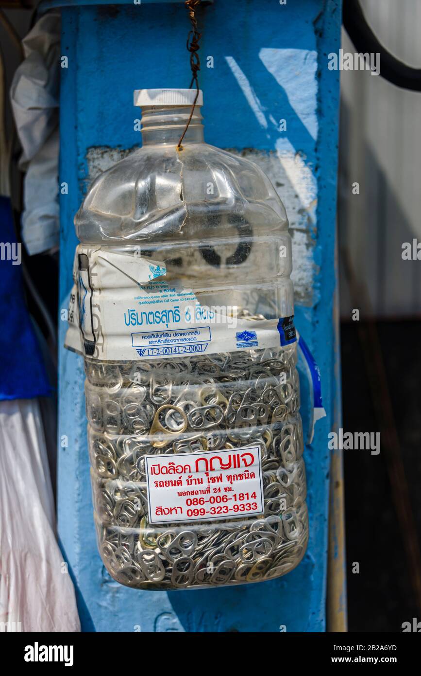 Bottiglia d'acqua in plastica contenente una raccolta di bevande può anelli tira, con un adesivo che fa pubblicità a un fabbro, Bangkok, Thailandia. Foto Stock