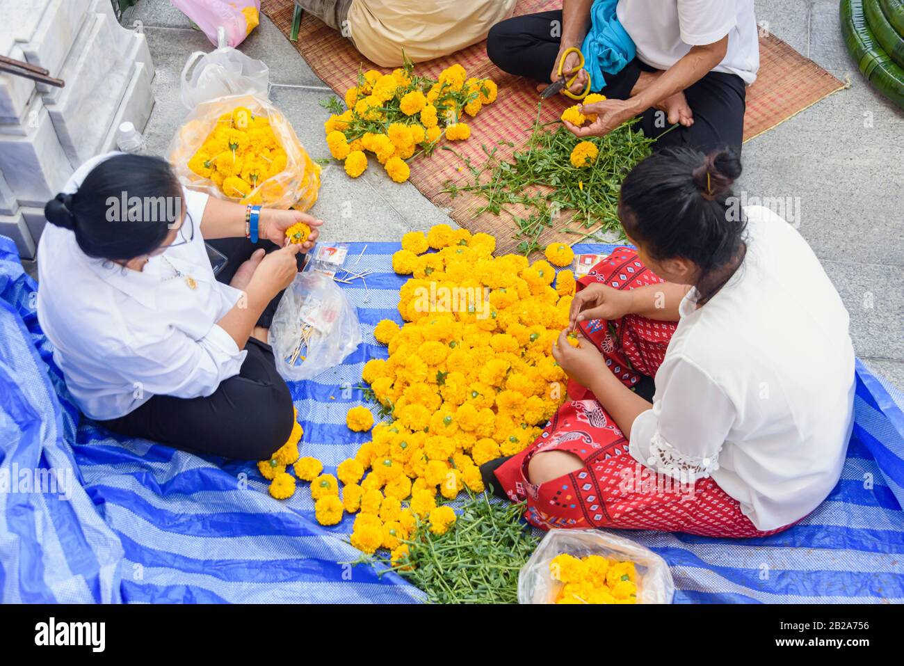 Donne filo ghirlande di fiori di crisantemo arancione pronto a decorare per il Capodanno cinese Lunar, a Wat Songkhram, Bangkok, Thailandia Foto Stock
