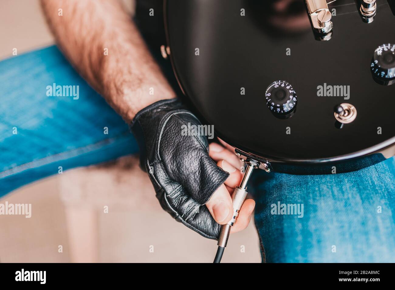 Un uomo in pelle nera guanti collega un cavo a una chitarra elettrica - plug and play Foto Stock