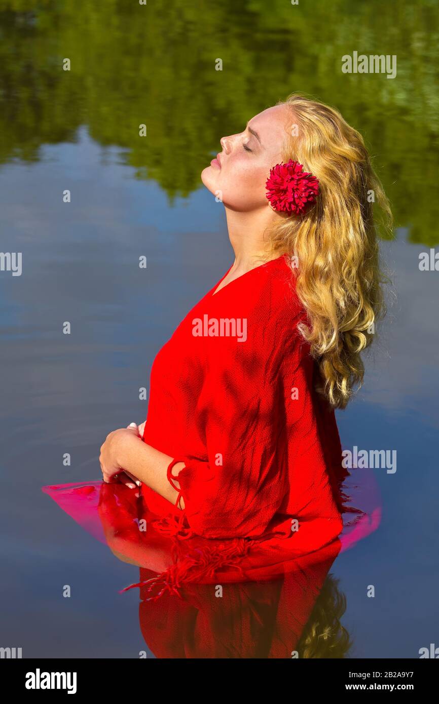 Attraente giovane bionda europea donna in abiti rossi si trova in acqua di fiume Foto Stock