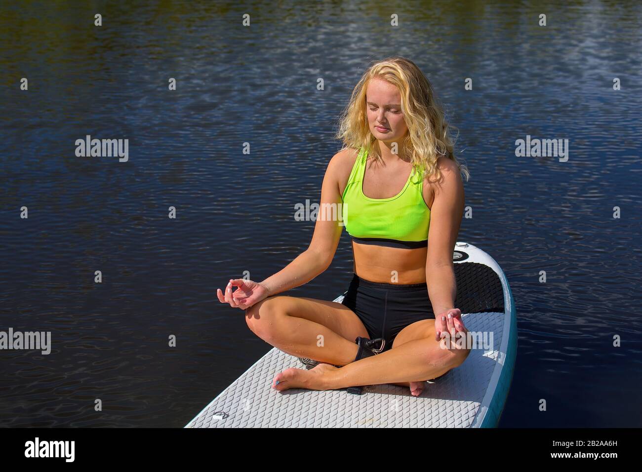 Giovane donna europea che medita con SUP sull'acqua nella natura Foto Stock
