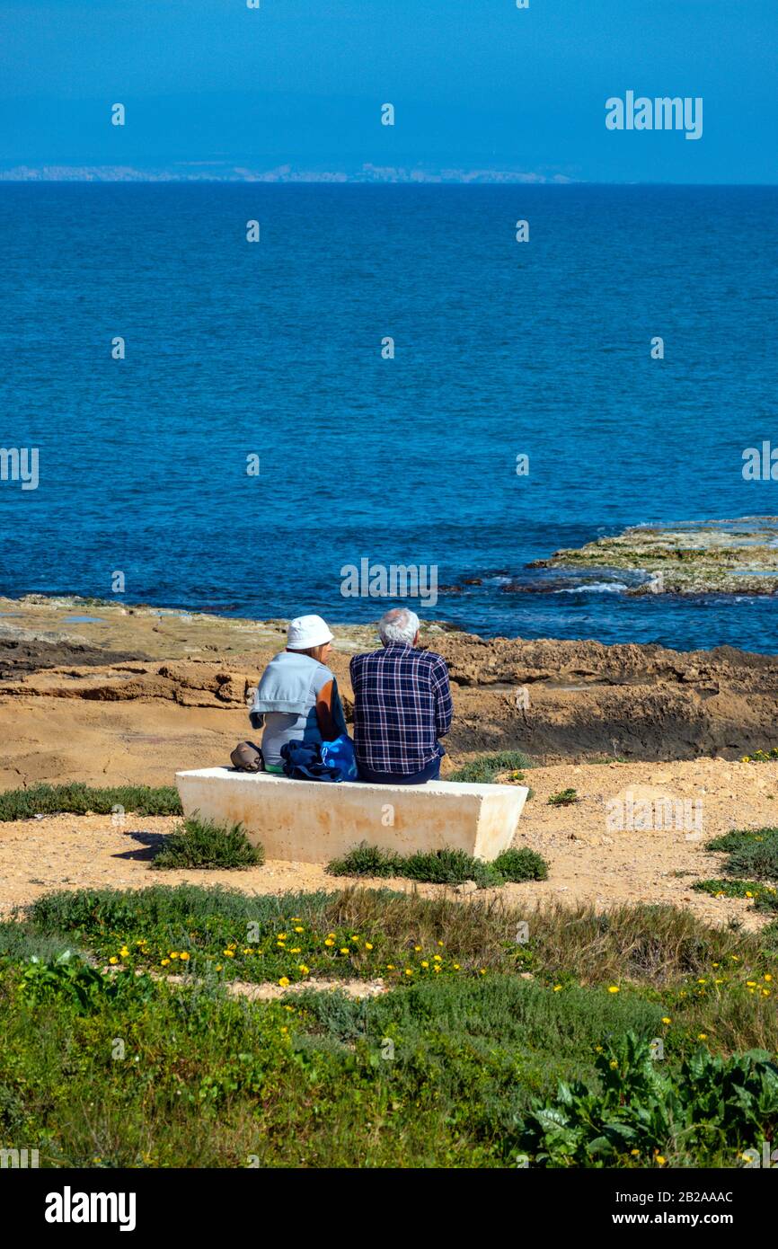 Due persone anziane sedute su panchina di cemento che guarda l'oceano, Torrevieja, Costa Blanca, Spagna Foto Stock