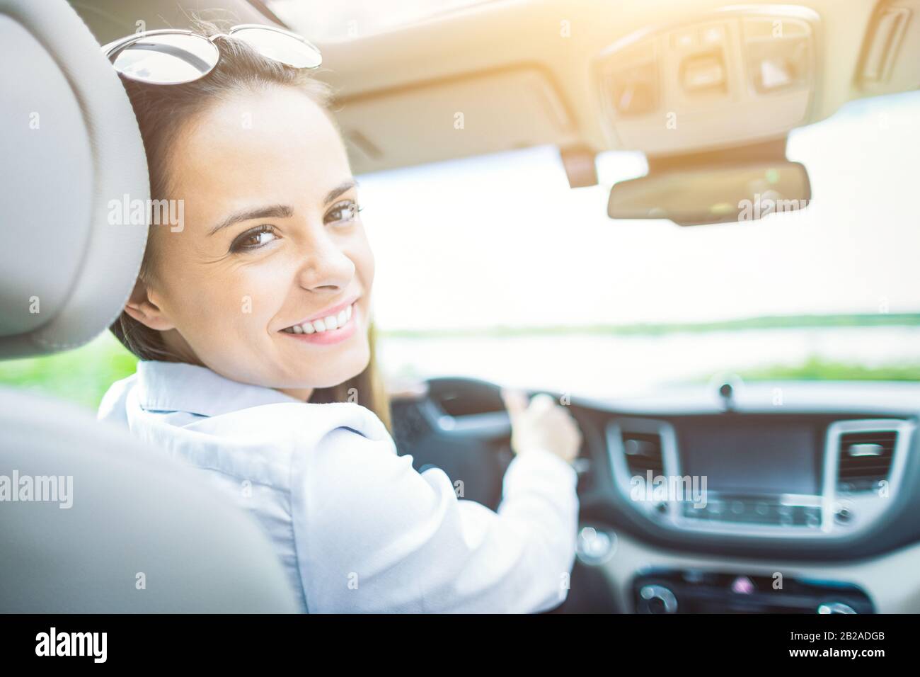 Bella giovane donna seduta all'interno di una nuova auto con un sorriso. È contento che sia un pilota. Foto Stock