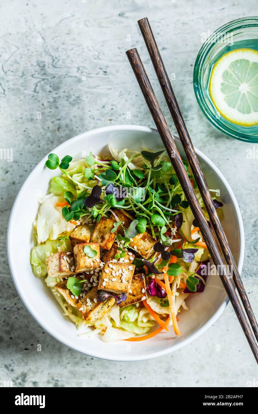 Insalata di tofu fritta con germogli e semi di sesamo in una ciotola bianca. Cibo vegano, cucina asiatica. Foto Stock