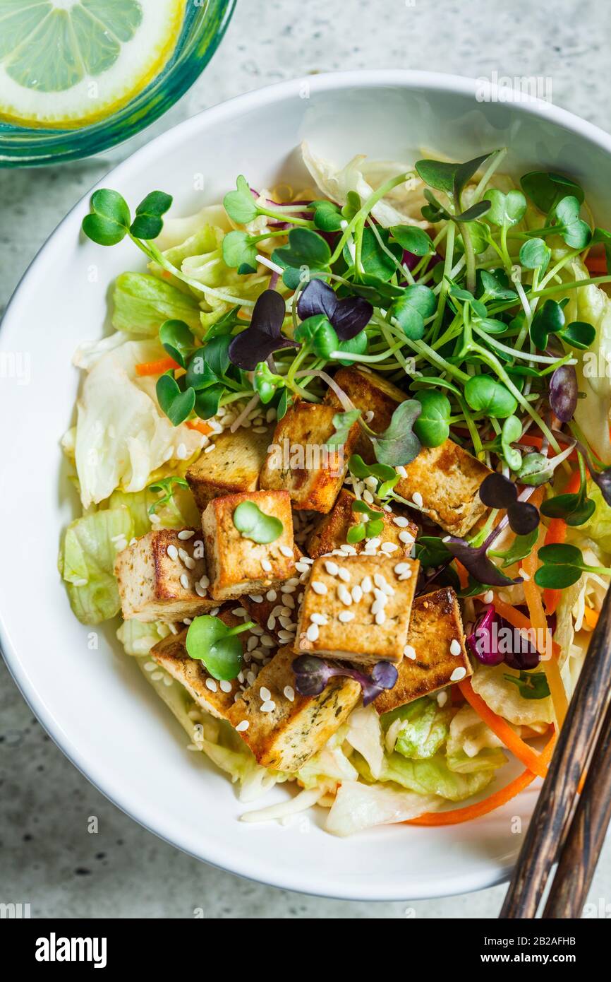 Insalata di tofu fritta con germogli e semi di sesamo in una ciotola bianca. Cibo vegano, cucina asiatica. Foto Stock