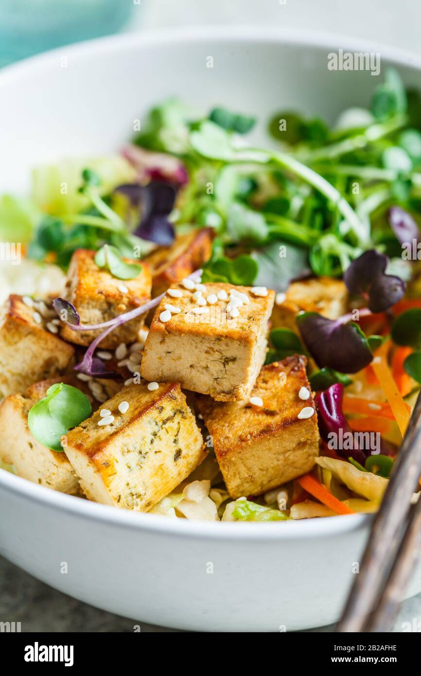Insalata di tofu fritta con germogli e semi di sesamo in una ciotola bianca. Cibo vegano, cucina asiatica. Foto Stock