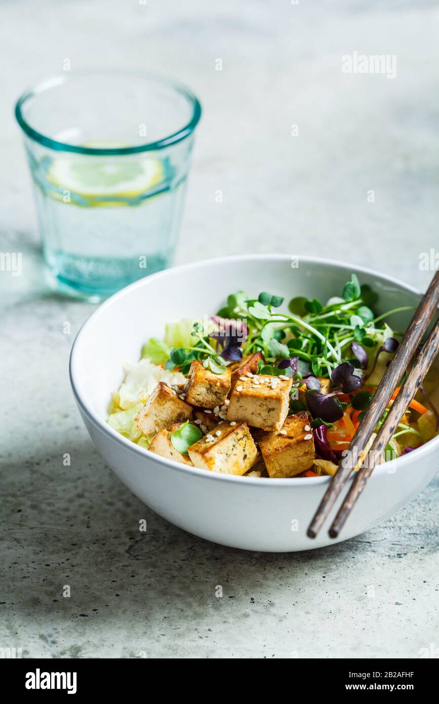Insalata di tofu fritta con germogli e semi di sesamo in una ciotola bianca. Cibo vegano, cucina asiatica. Foto Stock
