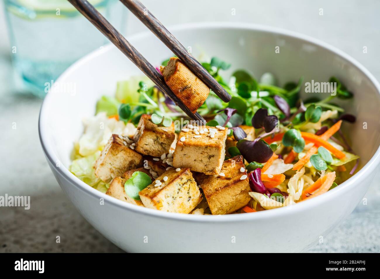 Insalata di tofu fritta con germogli e semi di sesamo in una ciotola bianca. Cibo vegano, cucina asiatica. Foto Stock