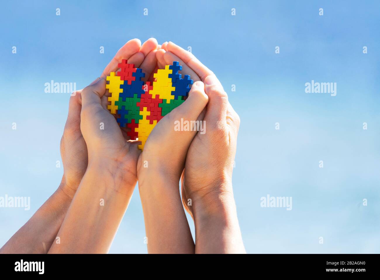 Mani per bambini e adulti che tengono il cuore colorato sullo sfondo blu del cielo. Mondo autismo concetto di giorno di consapevolezza Foto Stock