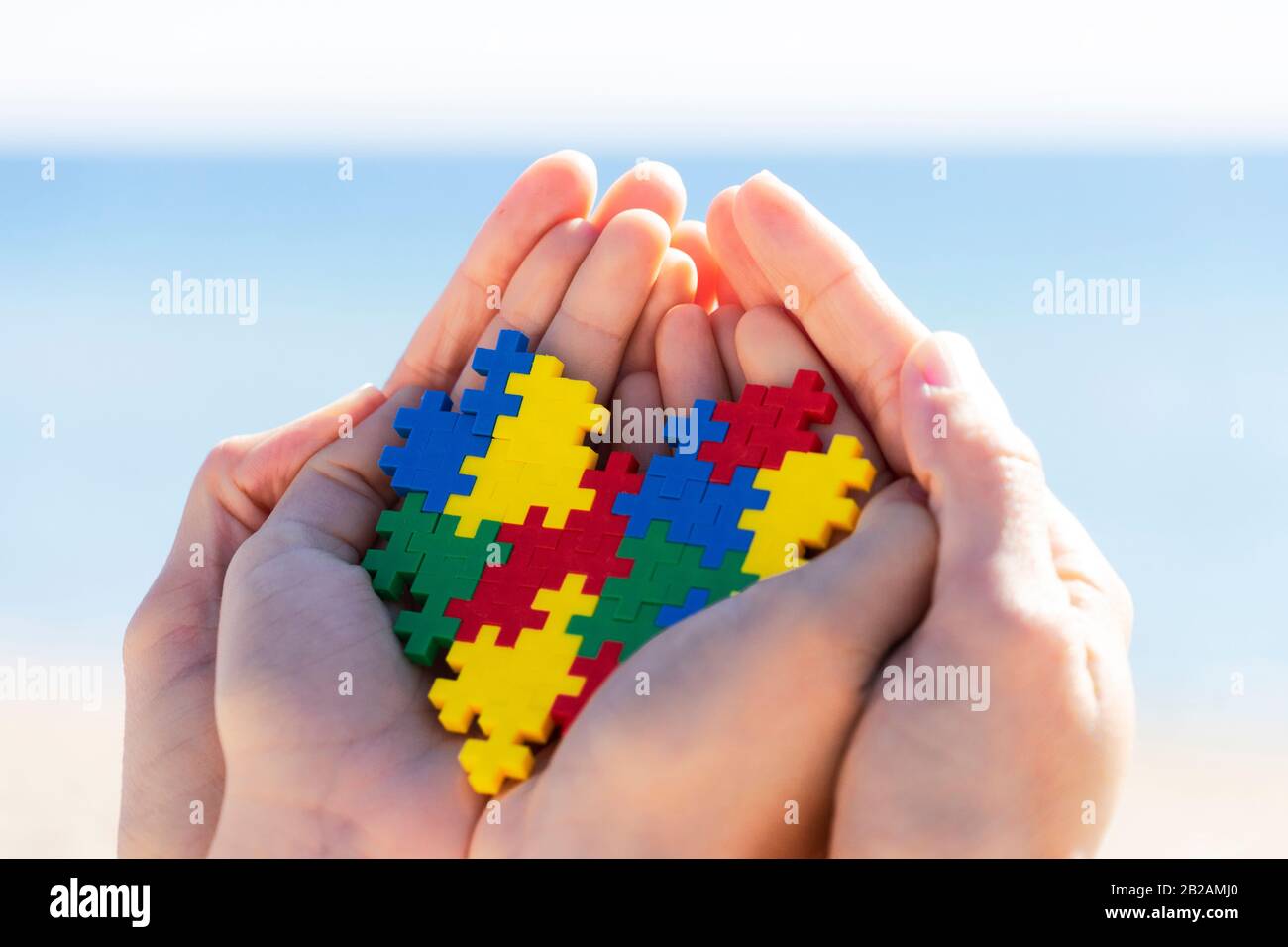 Mani per bambini e adulti che tengono il cuore colorato con sfondo blu all'aperto. Mondo autismo concetto di giorno di consapevolezza Foto Stock