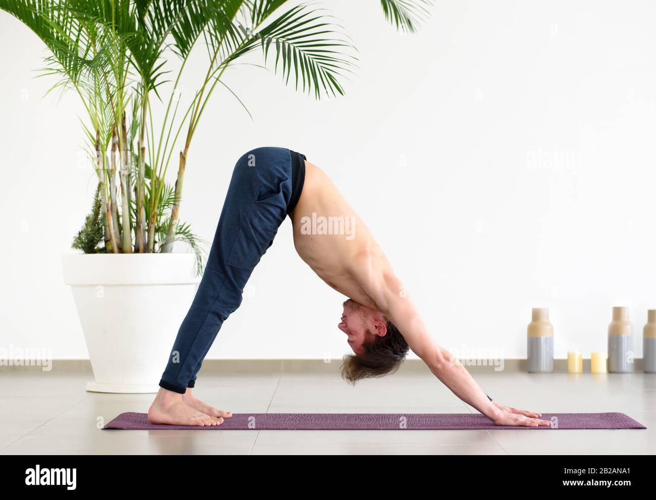 Supla misura l'uomo che fa una posa di yoga del cane rivolta verso il basso su un tappeto in una palestra chiave alta in una vista laterale di angolo basso per un concetto di salute e di idoneità Foto Stock