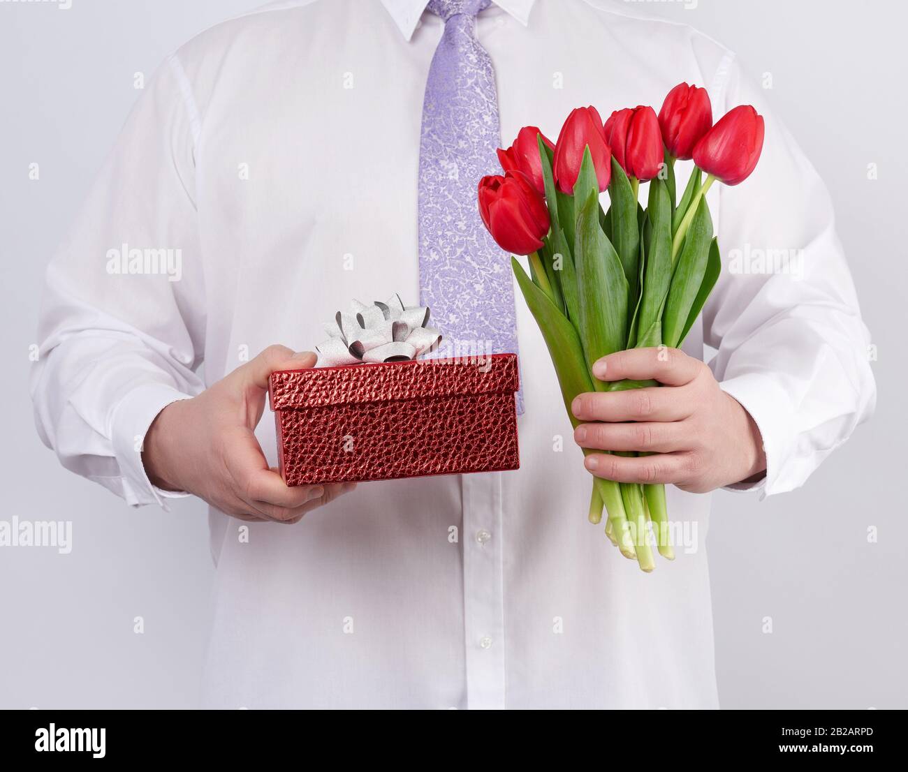 uomo adulto in camicia bianca e cravatta lilla con bouquet di tulipani  rossi con foglie verdi e scatola regalo su sfondo bianco, concetto per  felice Foto stock - Alamy