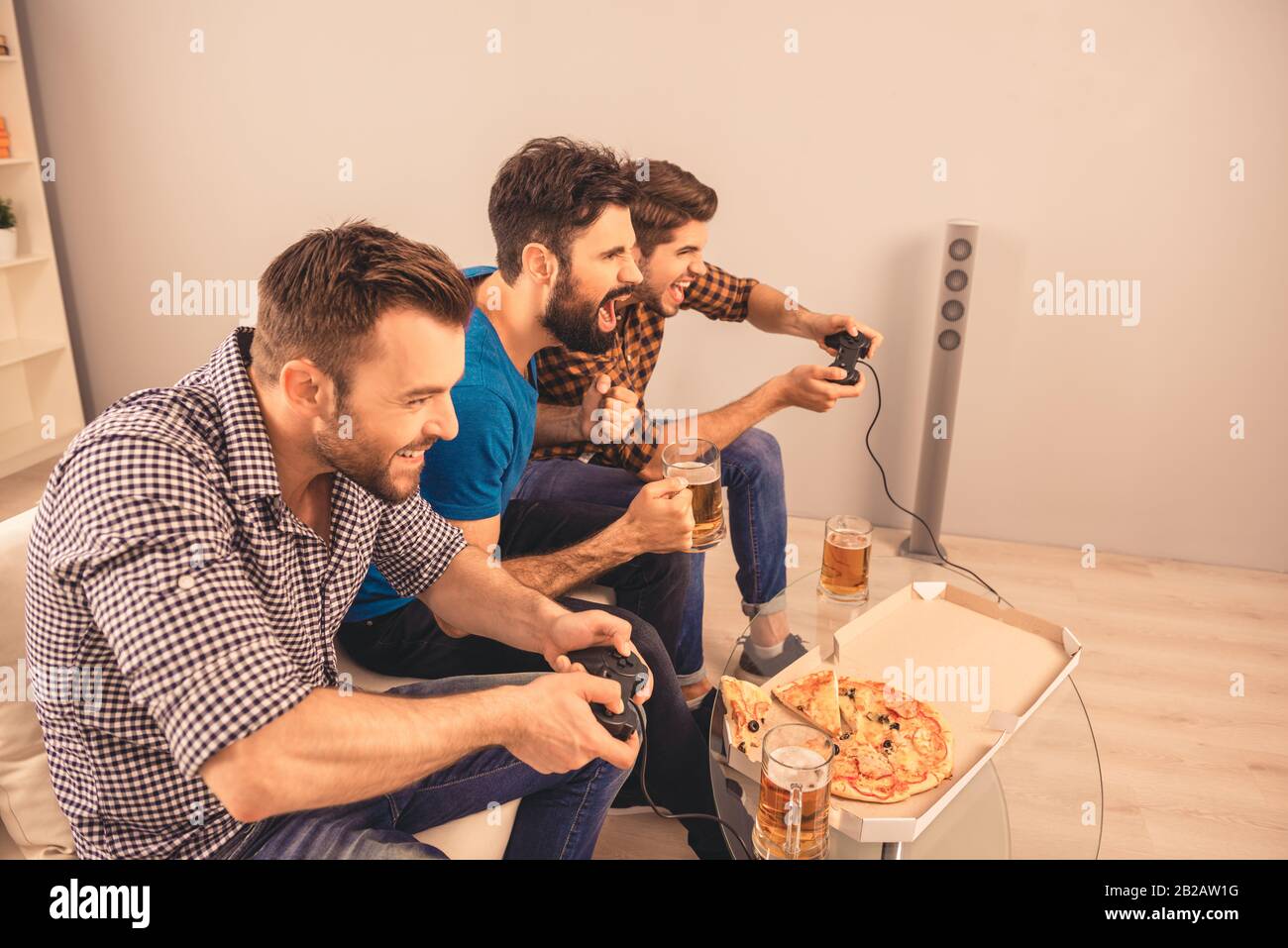 Tre uomini felici eccitati giocano a videogame con birra e pizza Foto Stock