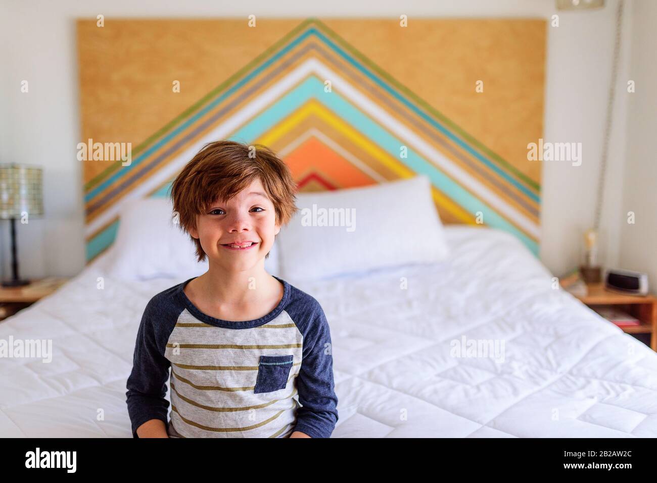 Ragazzo sorridente seduto sul bordo di un letto Foto Stock