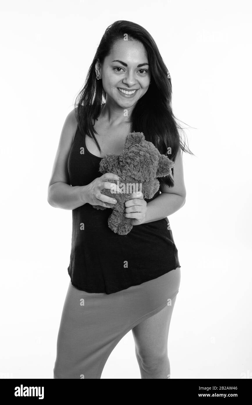 Studio shot di felice bella donna sorridente e in piedi tenendo orsacchiotto contro uno sfondo bianco Foto Stock