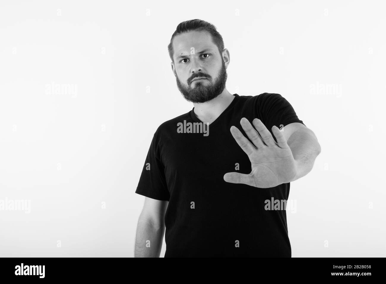 Studio shot del giovane uomo barbuto che mostra stop gesto mano contro uno sfondo bianco Foto Stock