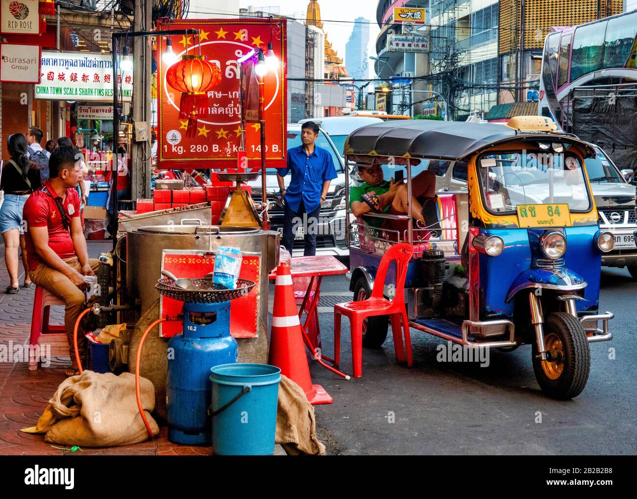 Tuk Tuk autista che riposa vicino ad una stalla di cibo di strada in Yaowarat Road, Bangkok, Tailandia Foto Stock