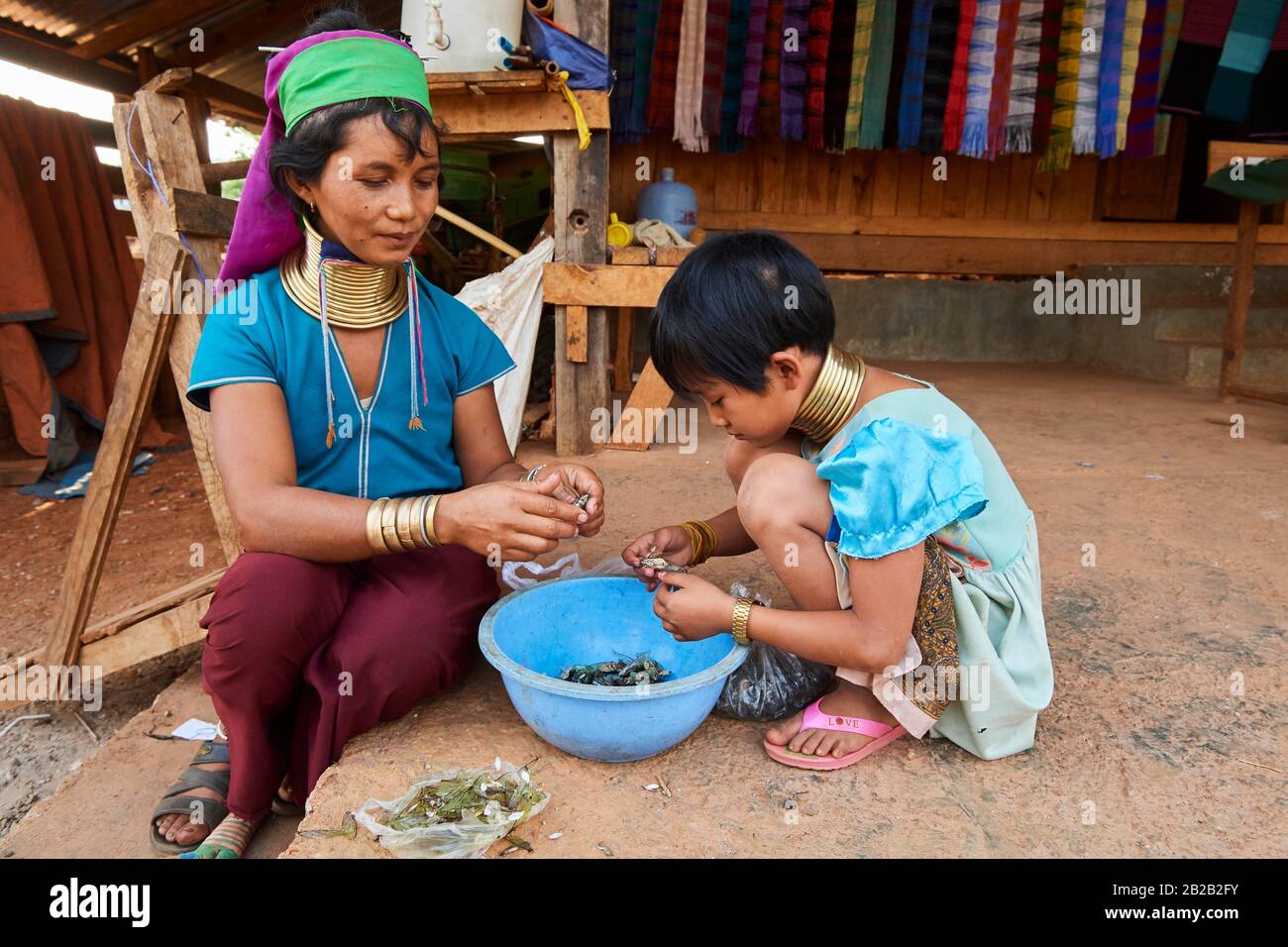 Kayan Lahwi donna con le bobine del collo di ottone e abbigliamento tradizionale con sua figlia. Stanno lavando e rimuovendo le ali dalle cicale che griglieranno Foto Stock