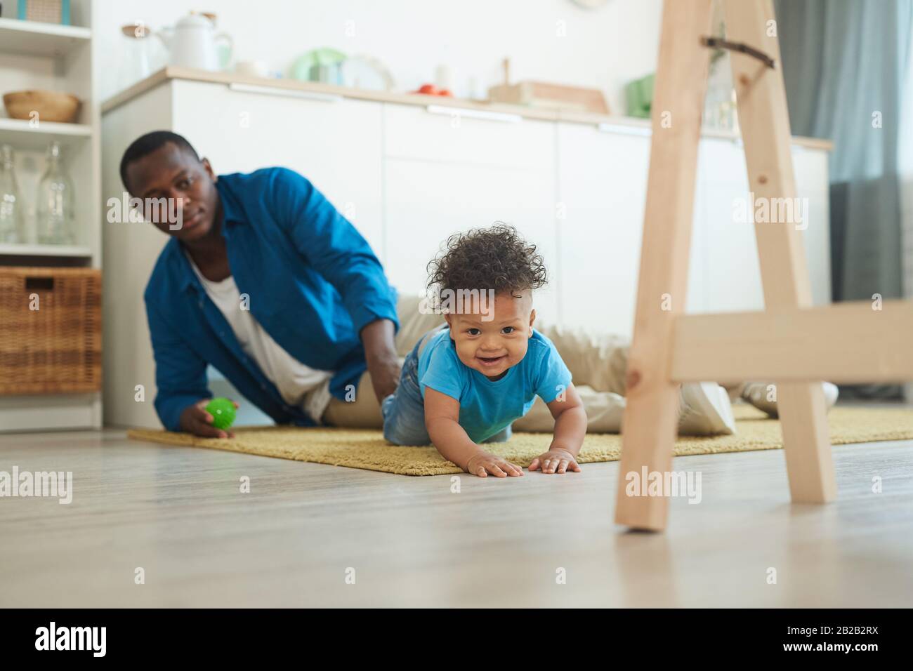 Ritratto di cute afro-americano toddler che strisciare sul tappeto mentre gioca con il dad a casa, copia lo spazio Foto Stock
