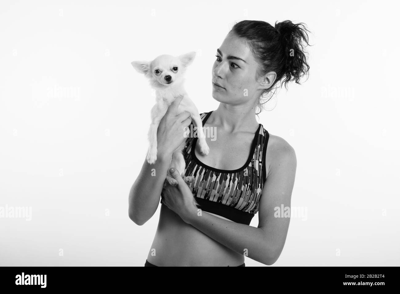 Studio shot della bella ragazza adolescente holding cute cane mentre lo sguardo scioccato pronto per sport ed esercizio contro uno sfondo bianco Foto Stock