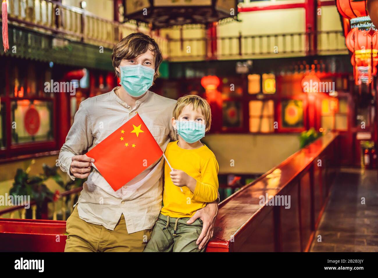 Godersi una vacanza in Cina. Turisti felici papà e figlio in maschera medica con una bandiera cinese su sfondo cinese. Viaggi in Cina con concetto di bambini Foto Stock