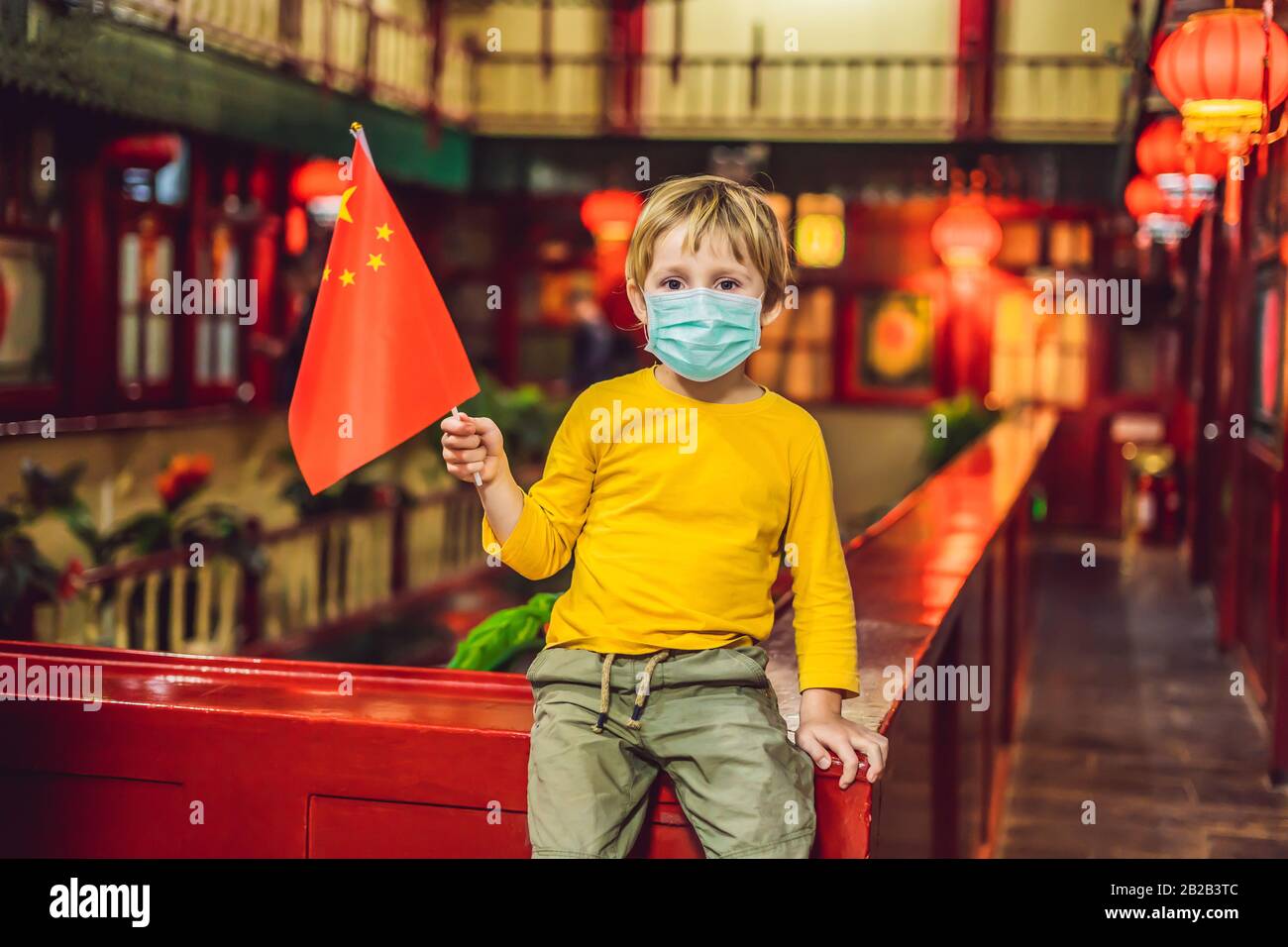 Godersi una vacanza in Cina. Felice ragazzo turistico in maschera medica con una bandiera cinese su sfondo cinese. Viaggi in Cina con concetto di bambini. Turisti Foto Stock