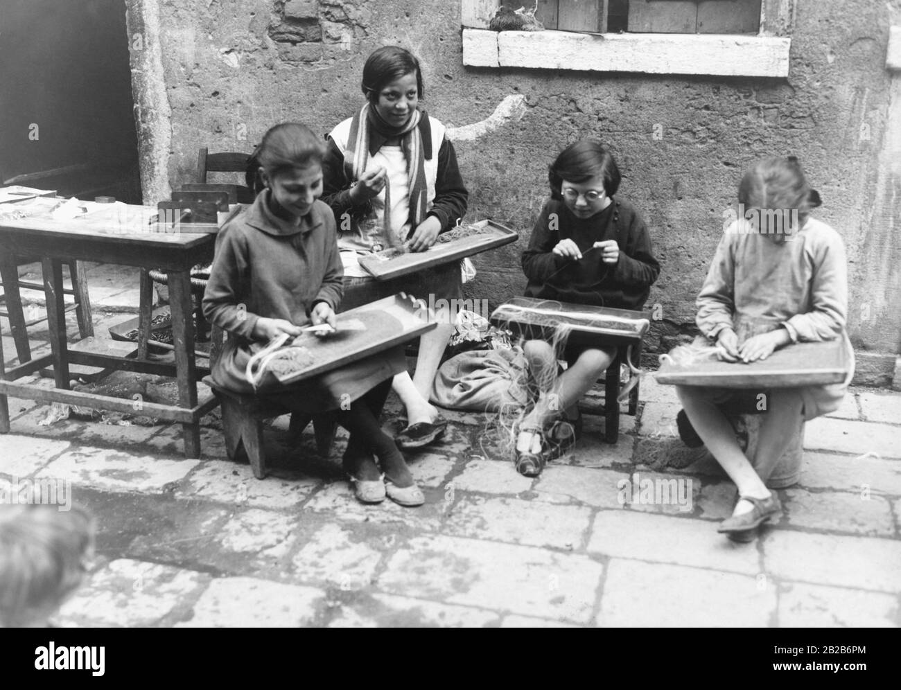 Bambini nel quartiere povero di Venezia che stringono perle su corde. Questo lavoro viene eseguito in condizioni di lavoro molto scarse. Foto Stock