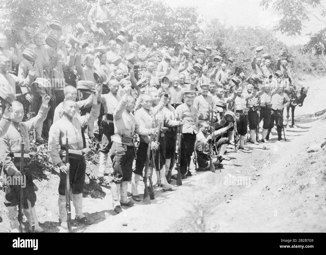 Soldati giapponesi in piedi sulla strada e ondeggiante con i loro tappi ad un generale in arrivo. Foto Stock