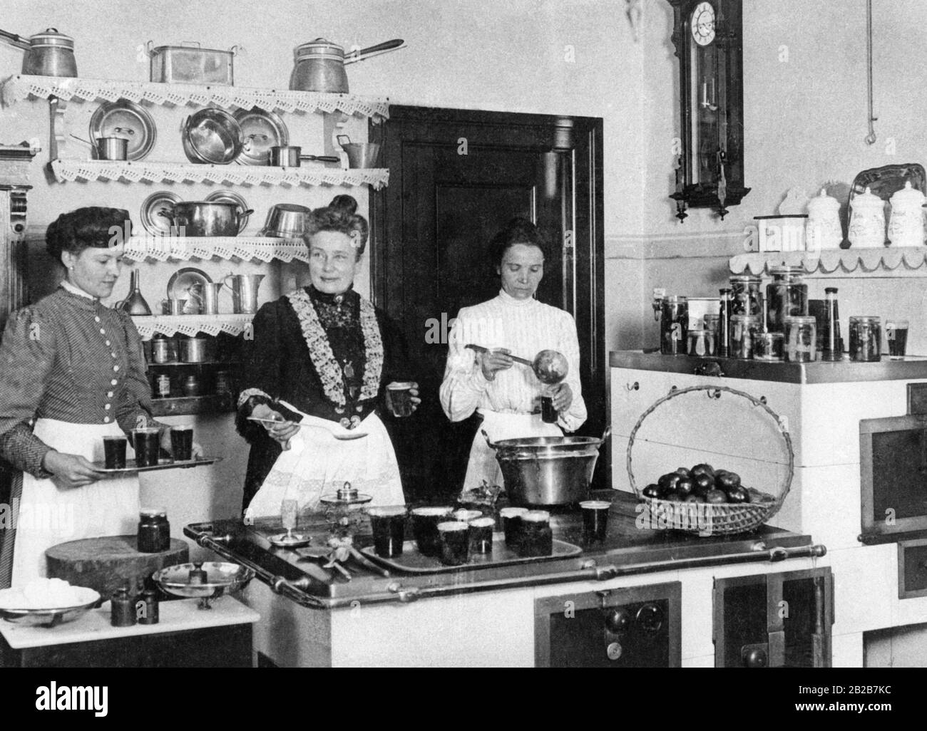 La grande stufa, di solito posta nel mezzo della cucina, dominava l'intero ambiente della classe media e superiore famiglia alla fine del secolo. Era il posto di lavoro centrale del cuoco e dei suoi aiutanti (qui quando conserva la frutta). In alto a destra sono presenti contenitori per farina, riso, panini, sale, ecc. Foto Stock