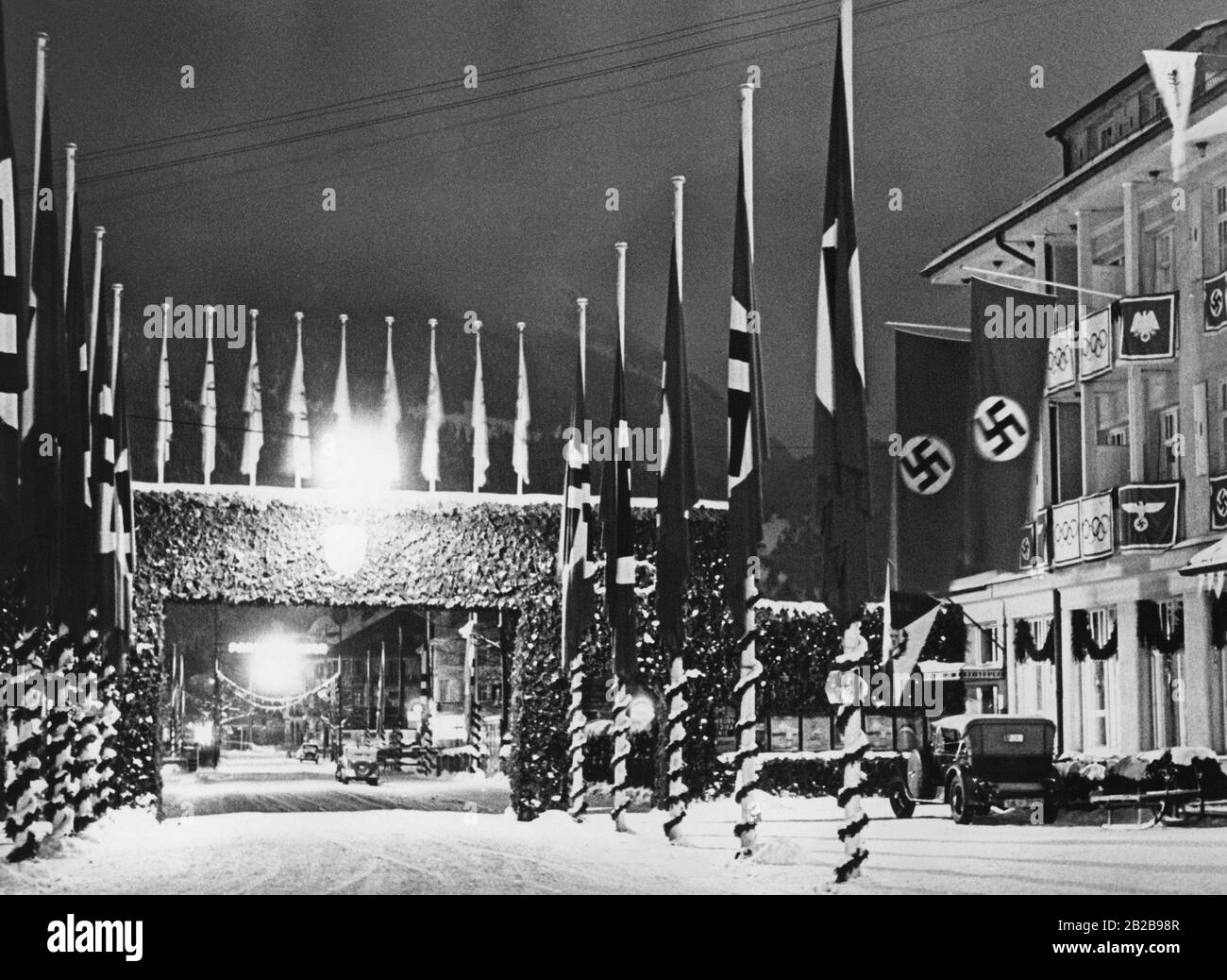 Vista sulla città di Garmisch-Partenkirchen dalla stazione ferroviaria. La strada è decorata con bandiere swastika e sul cancello d'ingresso alla città vecchia le bandiere olimpiche sono hoisted. Foto Stock
