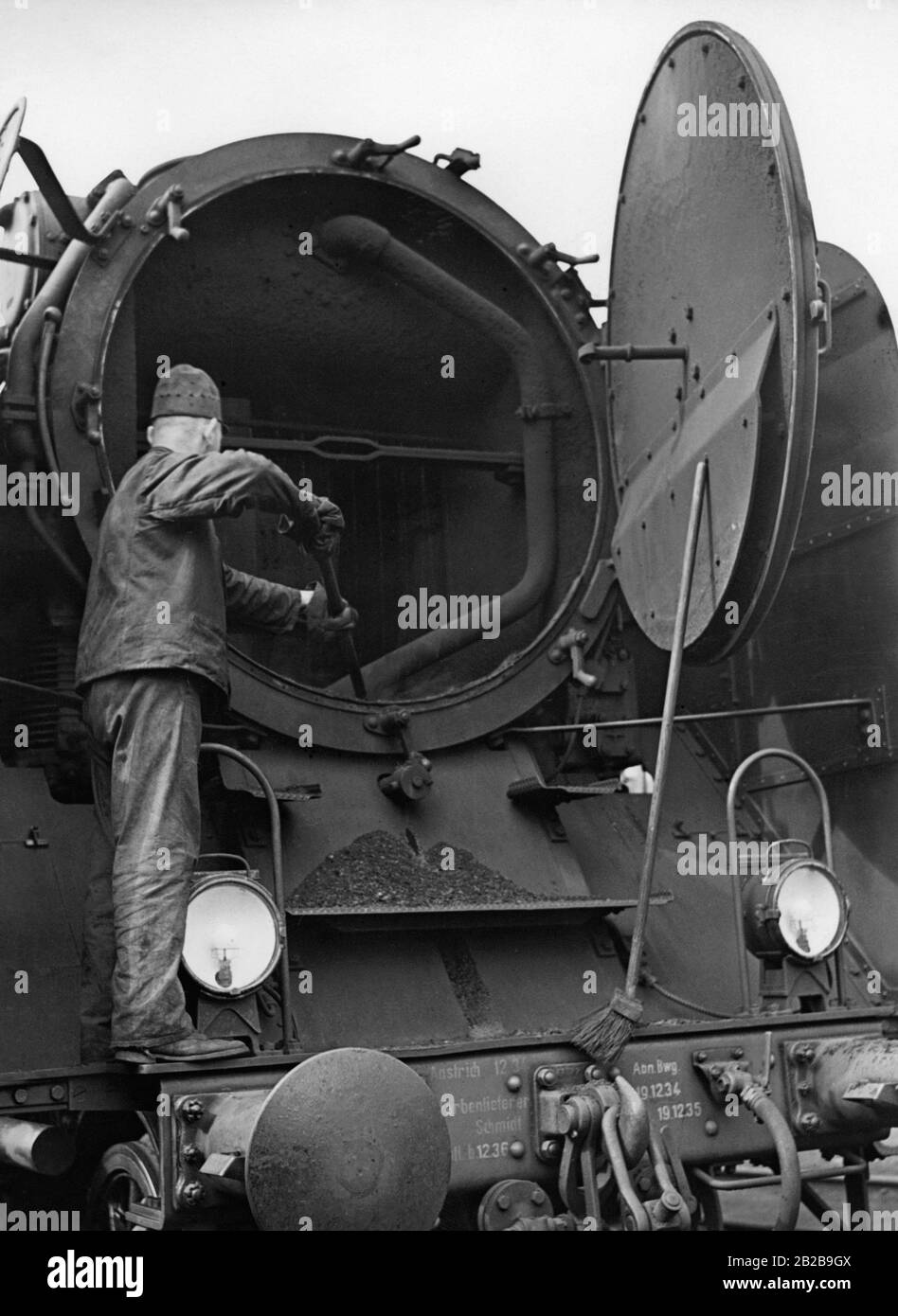 Operatore ferroviario durante la pulizia del fumatore di una locomotiva a vapore. Foto Stock