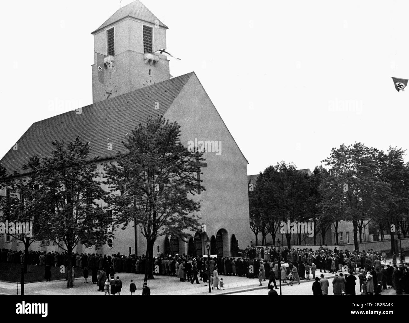 Una grande folla attende davanti alla Lindenkirche di Berlino-Wilmersdorf per l'inizio della consacrazione del servizio divino il 06.01.1936. Alla torre della chiesa è appesa una bandiera di Swastika. Foto Stock