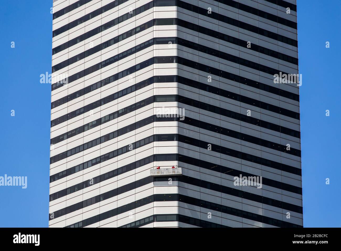 La facciata esterna dell'edificio degli uffici è stata ripulita da due operai sulla gru dell'ascensore. Lavoro di manutenzione ad alto rischio. Singapore. Foto Stock