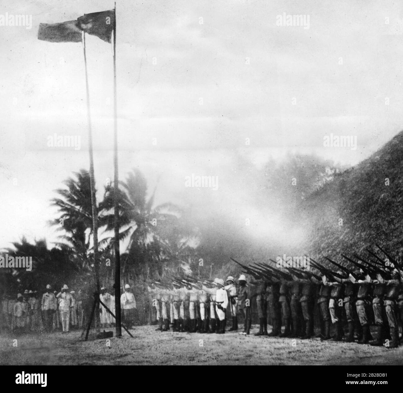Un saluto onorario alla bandiera di un dipartimento di polizia tedesco e di un gruppo di nativi Askaris durante la visita del governatore in un insediamento di missione all'interno dell'Africa orientale tedesca. Foto Stock