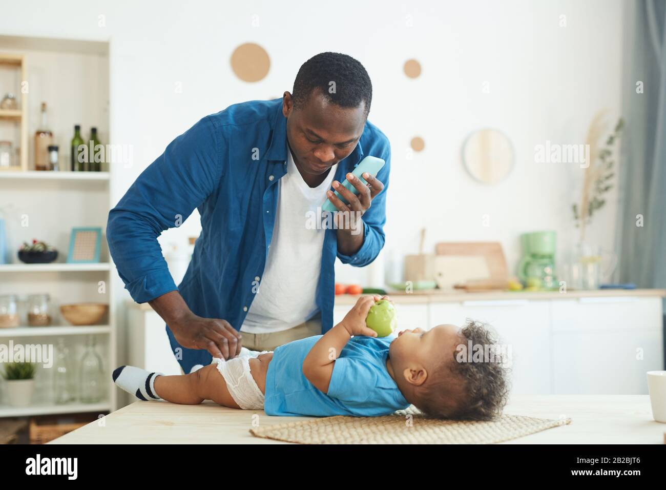 Ritratto di uomo africano-americano maturo che chiama moglie mentre cambia pannolino a bambino in casa interiore, copia spazio Foto Stock