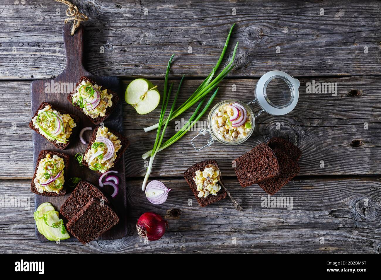 Aringa forshmak - cucina ebraica, su un pane di segale su un tagliere con ingredienti su un vecchio fondo di legno fienile, vista dall'alto, piatto lay, oriz Foto Stock