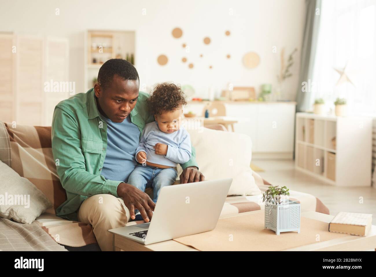 Ritratto di uomo africano-americano maturo che lavora sul laptop mentre il bambino di babysitting a casa, copia spazio Foto Stock