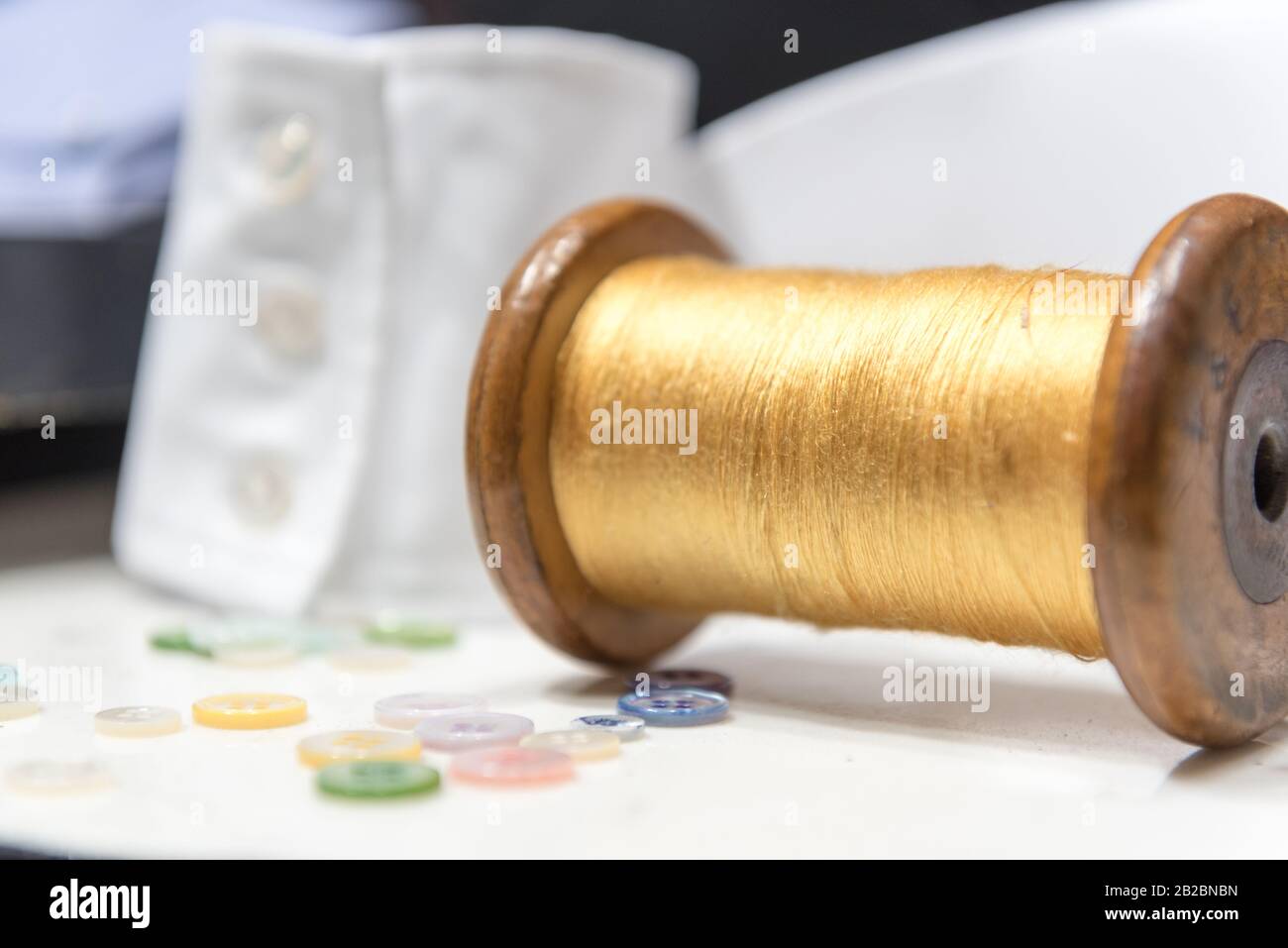 Bobina In Legno Con Filettatura Gialla Con Bottoni Assortiti E Bracciale Con Camicia Bianca Foto Stock