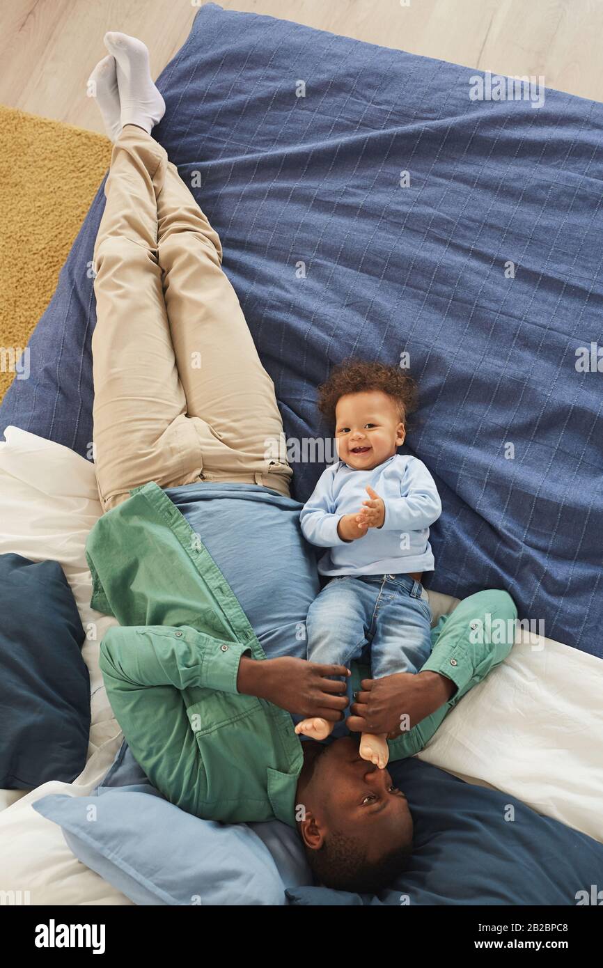 Ritratto della vista dall'alto dell'uomo afro-americano felice che gioca con il figlio cute del bambino mentre giace sul letto a casa, copia lo spazio Foto Stock