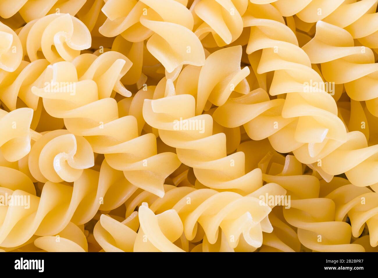 Pasta di fusilli essiccati crudi su dettagli di palo come sfondo giallo testurizzato. Pasta di grano rotini a forma di elica estrusa. Contengono saccaride, amido e glutine. Foto Stock