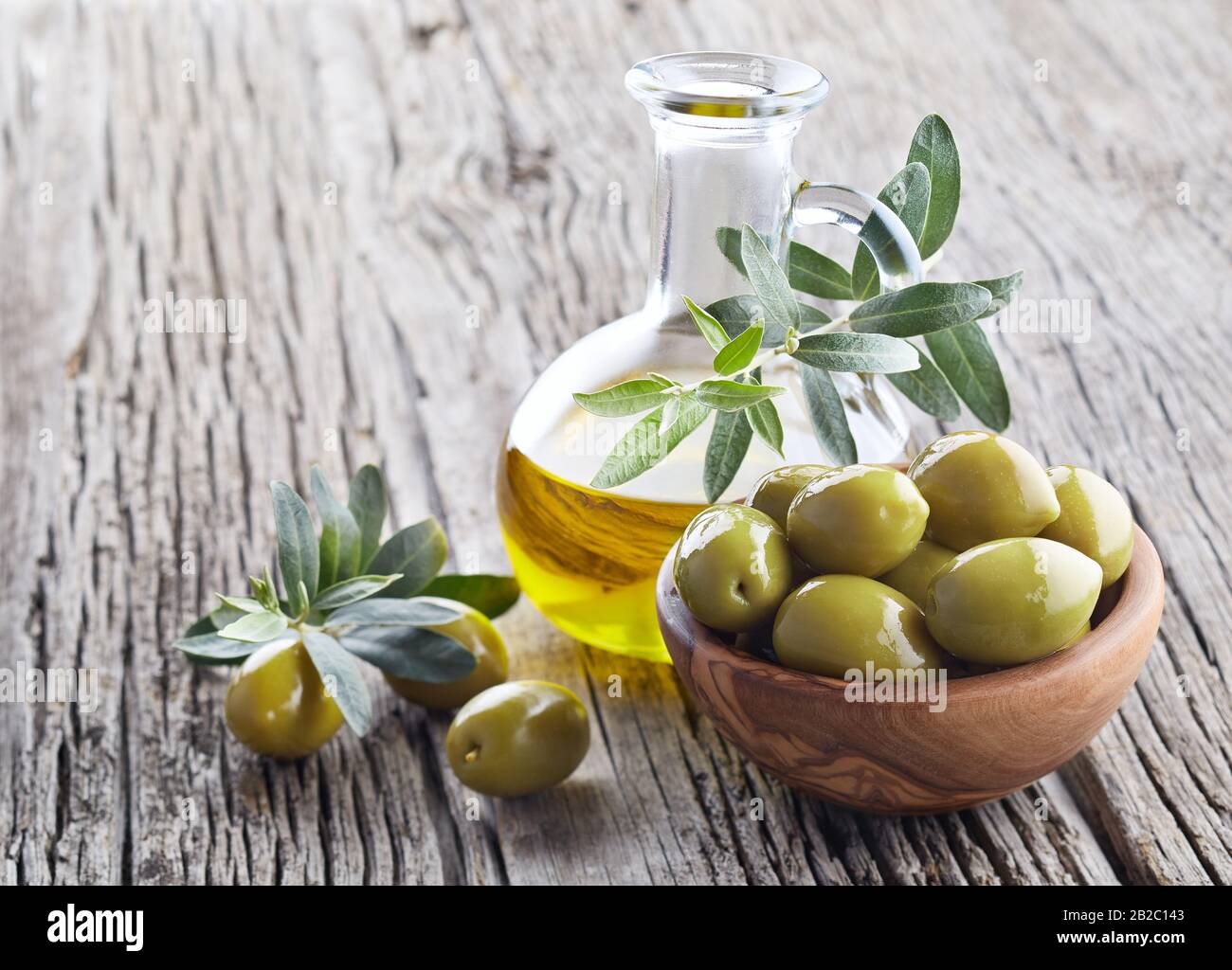 Olio di oliva vergine e olive verdi su tavola di legno Foto Stock