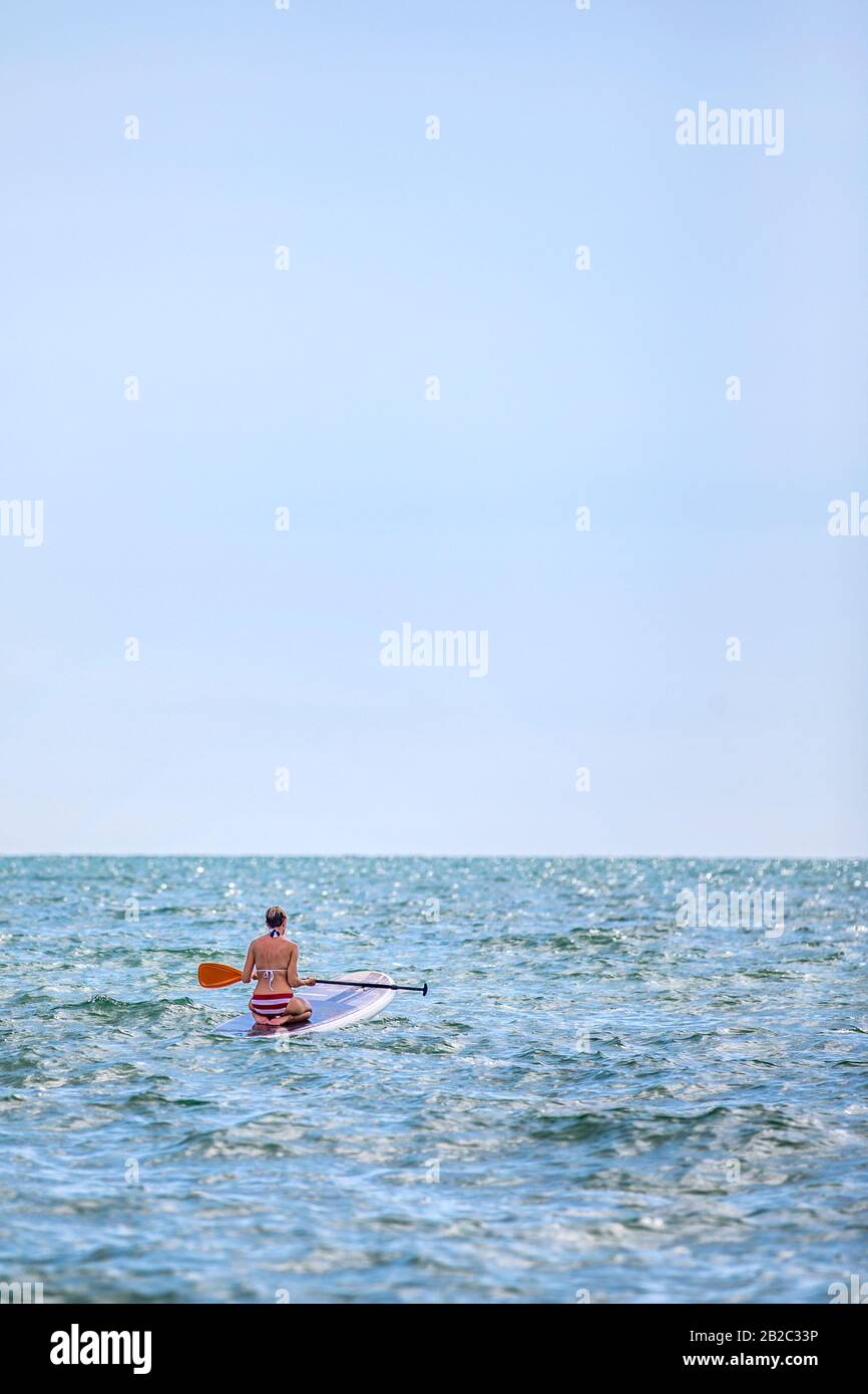 Creare fiducia. Una donna sta imparando come usare il suo SUP stand up paddle board inginocchiandosi su di esso prima di stare in piedi Beach vita a Napoli Florida Foto Stock