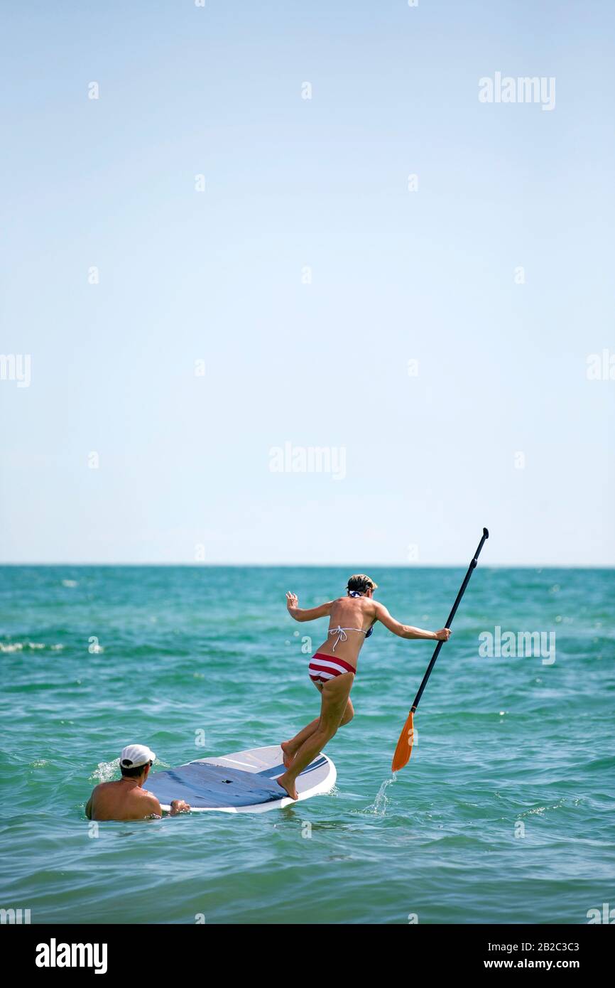 Le donne che imparano come usare una tavola SUP stand up paddle board ma perdere il suo equilibrio e saltare in acqua con una pagaia in mano. Giornata tropicale calda Foto Stock