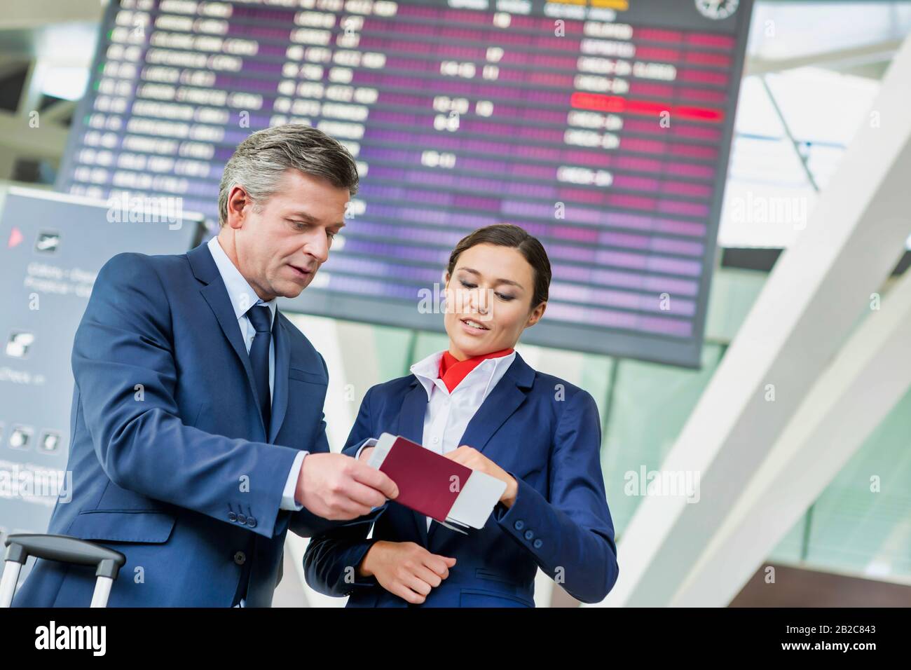 Un uomo d'affari maturo che mostra la sua carta d'imbarco con l'attraente personale dell'aeroporto Foto Stock
