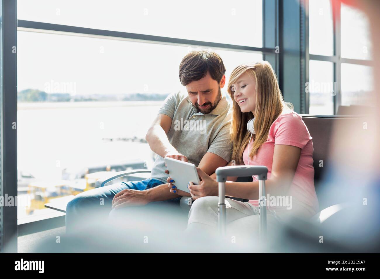 Ritratto di giovane bella ragazza teenage che mostra tablet digitale a suo padre mentre si siede e in attesa del loro volo in aeroporto Foto Stock