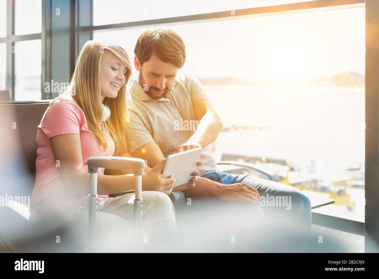 Ritratto di giovane bella ragazza teenage che mostra tablet digitale a suo padre mentre si siede e in attesa del loro volo in aeroporto Foto Stock