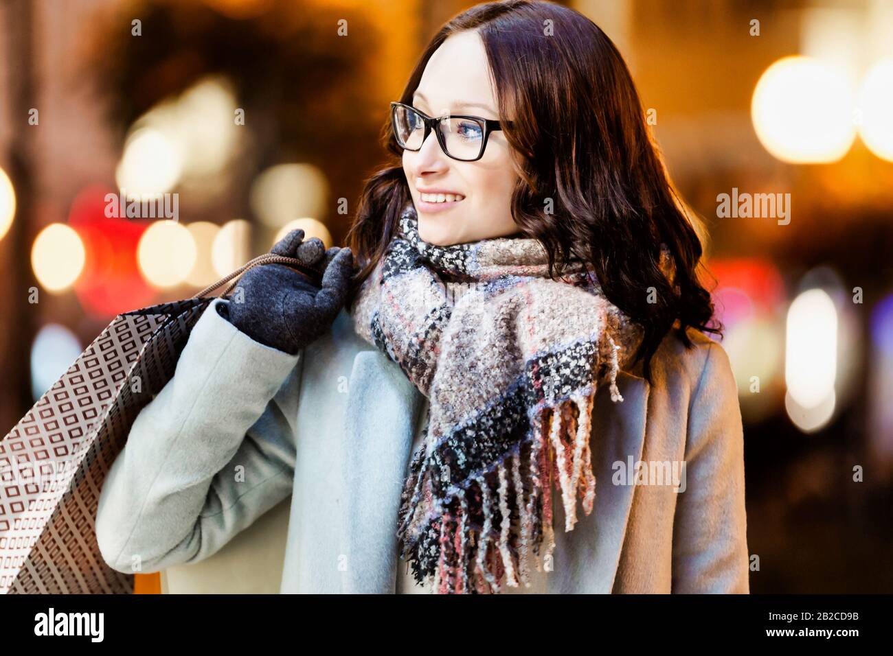 Ritratto di giovane donna attraente che cammina mentre tiene i sacchetti di carta sullo shopping di notte Foto Stock