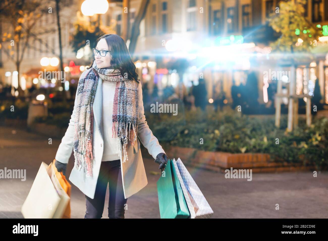 Ritratto di giovane donna attraente che cammina mentre tiene i sacchetti di carta sullo shopping di notte Foto Stock