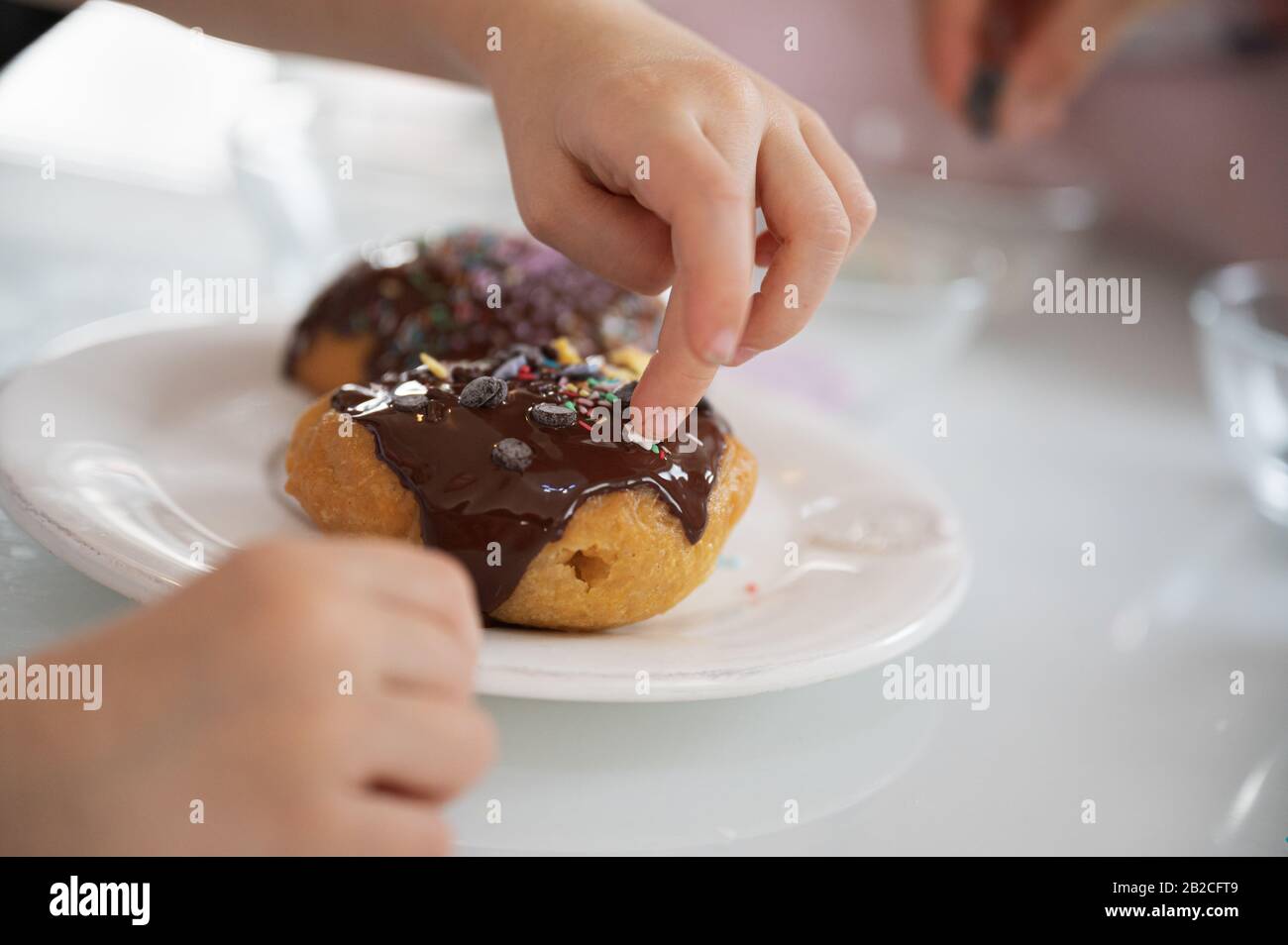 Closeup vista di un bambino che decorano una deliziosa casa fatta ciambella coperta di cioccolato con spruzzatori e stelle. Foto Stock